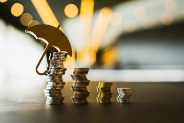 Model of umbrella and coins on wooden table concept of the system of insurance savings and the cost...
