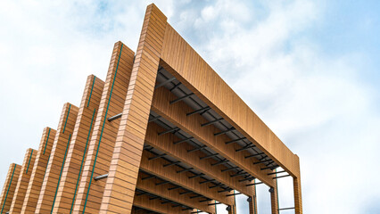 Modern wooden architectural design of outdoor stage with stacked beams and open spaces against a cloudy blue sky. Concept of contemporary architecture