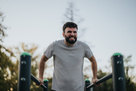 A man intensely exercising on parallel bars in a park. His expression shows determination and effort. The natural setting adds a refreshing element to the fitness routine.