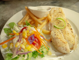 Fried fish fillet with french fries and salad on white plate