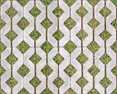 Geometric concrete paving stones with grass-filled gaps, arranged in a repetitive pattern on a flat surface. Seamless texture