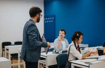 A teacher interacts with attentive students during a classroom session. The modern classroom has a vibrant blue wall and is equipped with desks and chairs for learning.