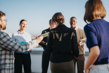 Obraz premium A group of multiracial business people gather on a rooftop at sunset, celebrating and sharing success. The scene exudes unity, diversity, and teamwork against a beautiful sky backdrop.