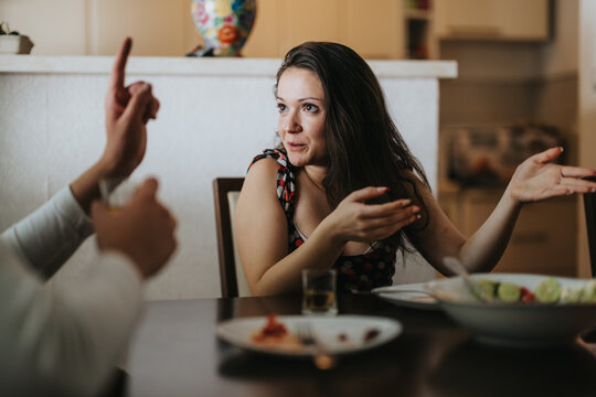 A woman passionately discusses a topic at the dinner table, using hand gestures to emphasize her point. The setting is cozy, highlighting a moment of connection and interaction.