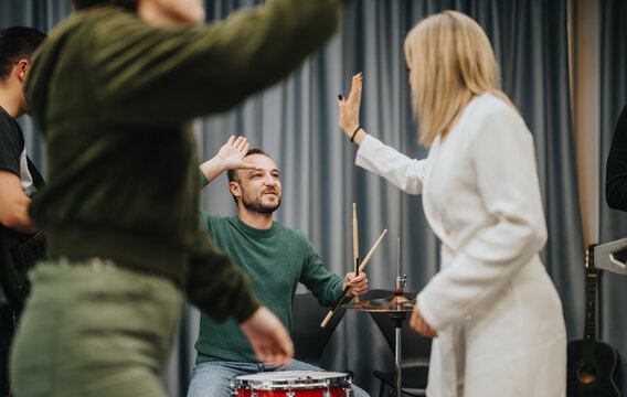 A diverse group of musicians energetically practicing in a music studio, focusing on collaboration and creativity. The drummer interacts with other band members, showing camaraderie and teamwork - Powered by Adobe