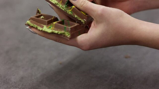 Female hands breaking off piece of Dubai chocolate on gray background. Green kadayif and pistachio spread with pistachio in trend dessert. Close-up, selective focus. High quality 4k footage