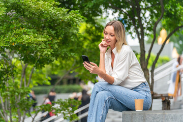 Caucasian Woman Sitting and Using Phone While Having a Cup of Coffee Outdoor a Park