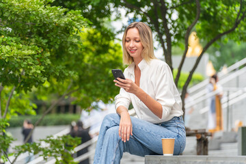 Caucasian Woman Sitting and Using Phone While Having a Cup of Coffee Outdoor a Park