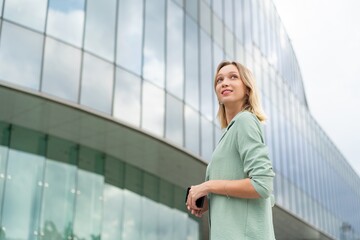 Caucasian Businesswoman Using Phone In Front A Modern Glass Office Building In the City