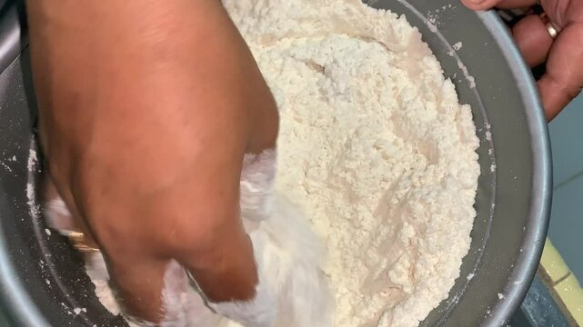 A hand mixing flour in a bowl, likely for baking or cooking purposes.