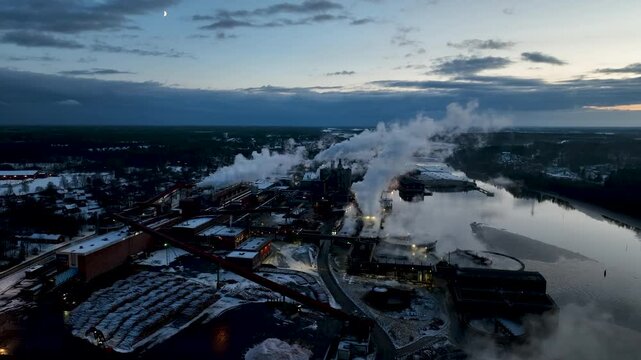 Aerial view of smoke plumes billowing from industrial paper mill chimneys at sunset