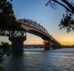 Obraz premium Auckland Harbour Bridge framed by Pohutukawa trees at sunset.