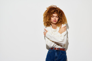 Young woman with curly hair expressing discomfort against a plain white background, dressed in a...
