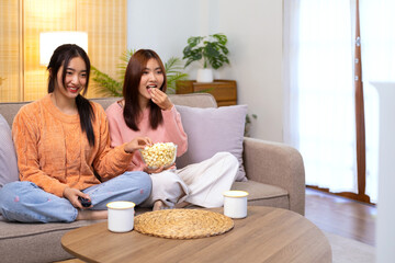 Wondered amazed impressed girl gesturing forefinger eating popcorn watching funny comic program with friend sitting in living room indoor enjoying interesting film