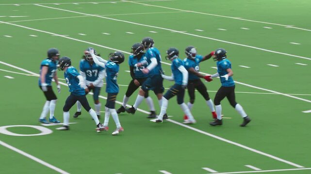 Excited Diverse Team of American Football Players Walking on Stadium Field. Team of Footballers in Blue Jerseys Celebrating a Victory, Raising Arms, Motivating Emotional Sports Fans