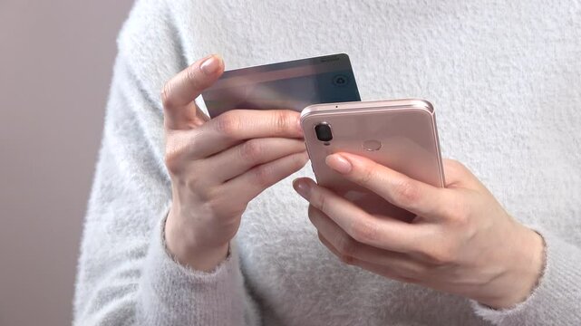 クレジットカードを持ち、スマートフォンでカード情報を入力する女性の手元のクローズアップ  4K