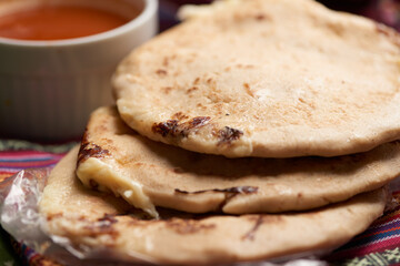 Pupusas with curtido and sauce served on a tamale leaf atop a wooden surface, highlighting traditional Central American flavors.