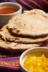 Pupusas with curtido and sauce served on a tamale leaf atop a wooden surface, highlighting traditional Central American flavors.