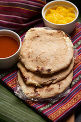 Pupusas with curtido and sauce served on a tamale leaf atop a wooden surface, highlighting traditional Central American flavors.