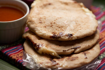 Pupusas with curtido and sauce served on a tamale leaf atop a wooden surface, highlighting traditional Central American flavors.