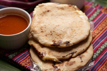 Pupusas with curtido and sauce served on a tamale leaf atop a wooden surface, highlighting traditional Central American flavors.