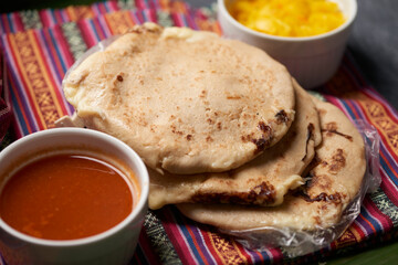 Pupusas with curtido and sauce served on a tamale leaf atop a wooden surface, highlighting traditional Central American flavors.