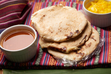 Pupusas with curtido and sauce served on a tamale leaf atop a wooden surface, highlighting traditional Central American flavors.