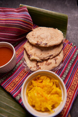 Pupusas with curtido and sauce served on a tamale leaf atop a wooden surface, highlighting traditional Central American flavors.