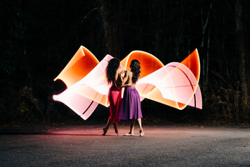 Two women standing together with vibrant light trails at night