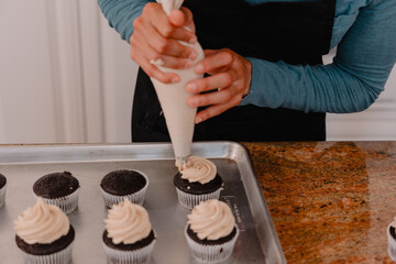 Baker using pastry bag to add vanilla cupcake to cupcakes