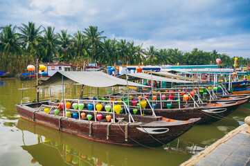 Obraz premium Colorful traditional Vietnamese boats decorated with lanterns lined up on the riverbank in Hoi An