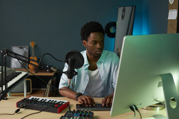 Producer sitting at his workplace and using computer to make song in record studio