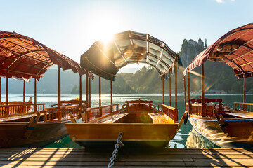 Traditional pletna boats waiting on lake bled at sunrise with bled castle in background