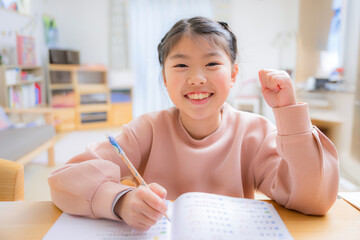 カメラ目線で笑顔で勉強をする小学生の女の子　ガッツポーズ