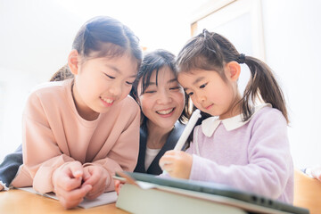 メインビジュアルにも！逆光の中、勉強や宿題をみるお母さんや塾の先生　小学生低学年の笑顔の子供「タブレットでも勉強楽しい」クローズアップ