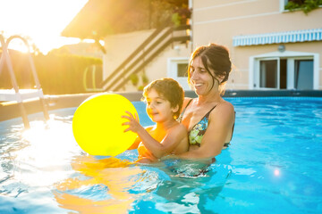 Mother and son playing with inflatable ball in swimming pool during summer vacation