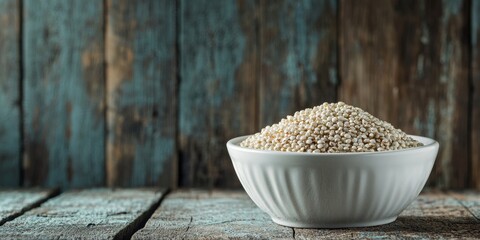 White quinoa grain in a white bowl is beautifully displayed over a rustic wooden background, highlighting the natural texture and color of the white quinoa grain in an appealing way.