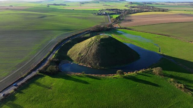Aerial shot flying over countryside at sunset towards Silbury Hill