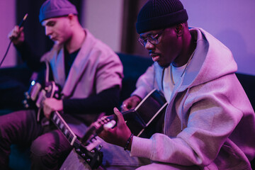 Two multiracial musicians playing electric guitars indoors, showcasing creativity and collaboration. The relaxed environment and casual attire emphasize a laid-back, artistic vibe.