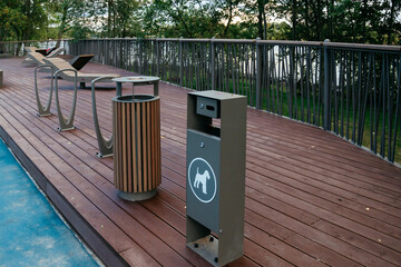 container for dog waste in public park. public place for walking with urns and sun loungers. wooden flooring on the floor in public park. cleaning for pets, ecology