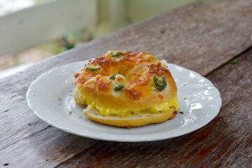 Fresh bagel with cheese, chili, and scrambled egg in a white dish on a wooden background.