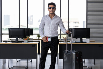 Handsome business man holding passport and luggage in workplace of office. Summer vacations concept.