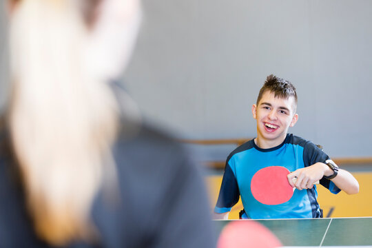 Happy disabled boy playing table tennis with coach at sports court