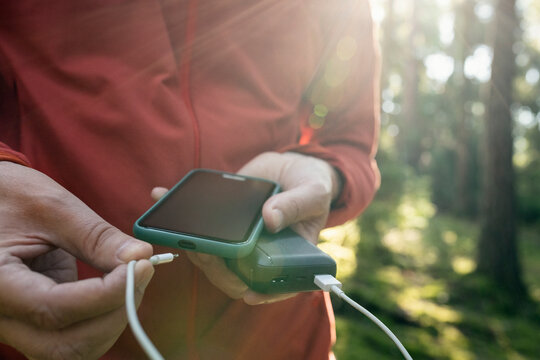 Midsection of man charging phone with power bank while hiking in forest