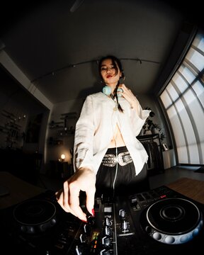 close-up perspective of a DJ's hands adjusting knobs and sliders on a professional DJ mixer with vibrant lighting, capturing the focus and precision of the performance.