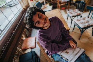 A young man with headphones sits in a cozy cafe, lost in music and relaxation. He enjoys a peaceful moment away from daily stress, with a notebook beside him.