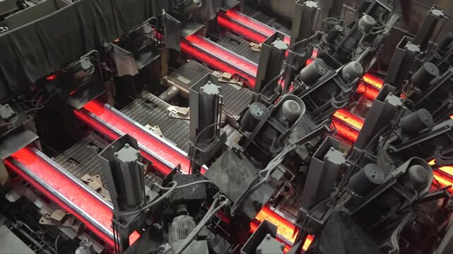 Witness the intense process of hot steel billets being transported on a conveyor in a steel mill. The glowing metal highlights the industrial operation.