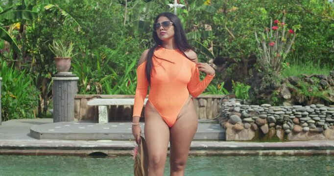 Near a pool reflecting a striking castle, a girl in an orange bikini basks in the sun.
