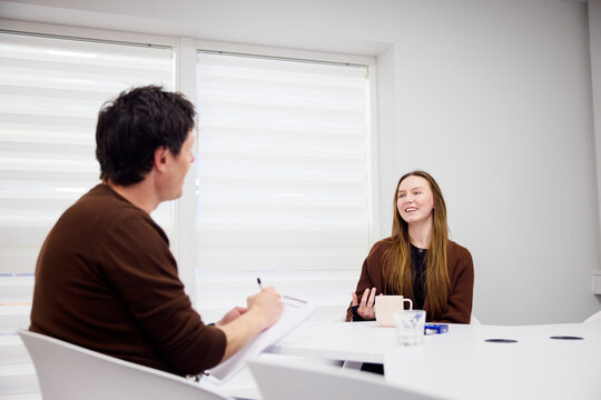 Smiling young woman talking with male medical professional during interview in office