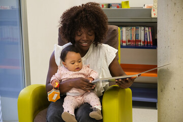 Mother reading a book to her baby daughter in the library